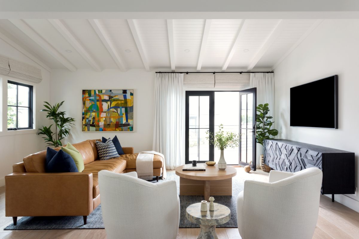 Living room with beamed ceiling, cognac leather sofa, white swivel chairs and abstract canvas