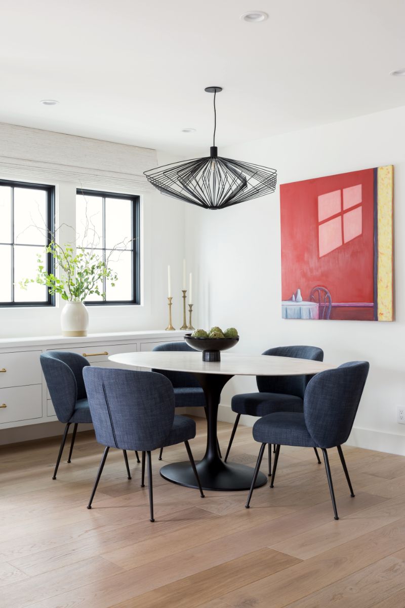 Dining area with navy velvet chairs, marble tulip table and red abstract art