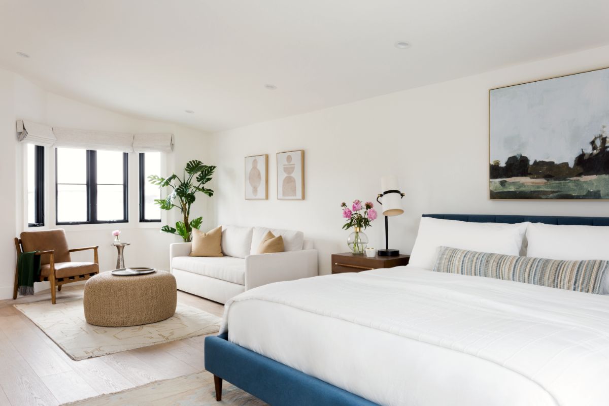 Bedroom with navy upholstered bed, landscape painting and leather lounge chair