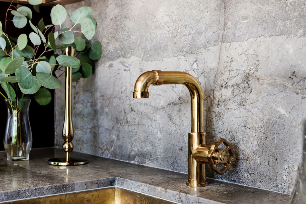 Brass bar faucet against a stone slab backsplash